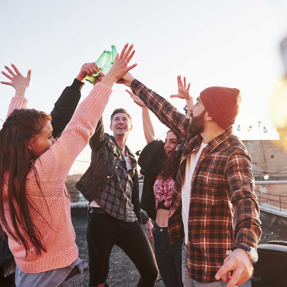 JGA_0005_decorative-festive-light-bulbs-holidays-on-the-rooftop-cheerful-group-of-friends-raised-their-hands-up-with-alc